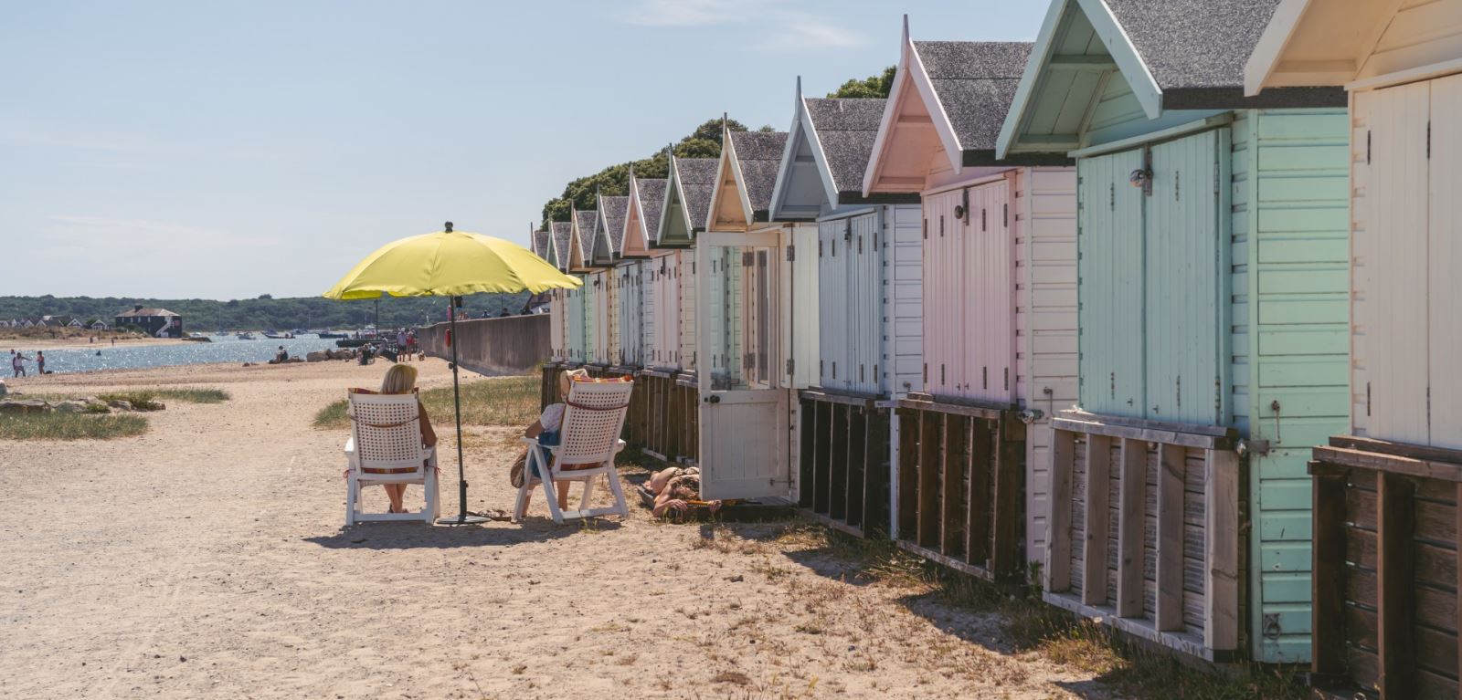 Couple relaxing in deck chairs next to the colourful beach huts 